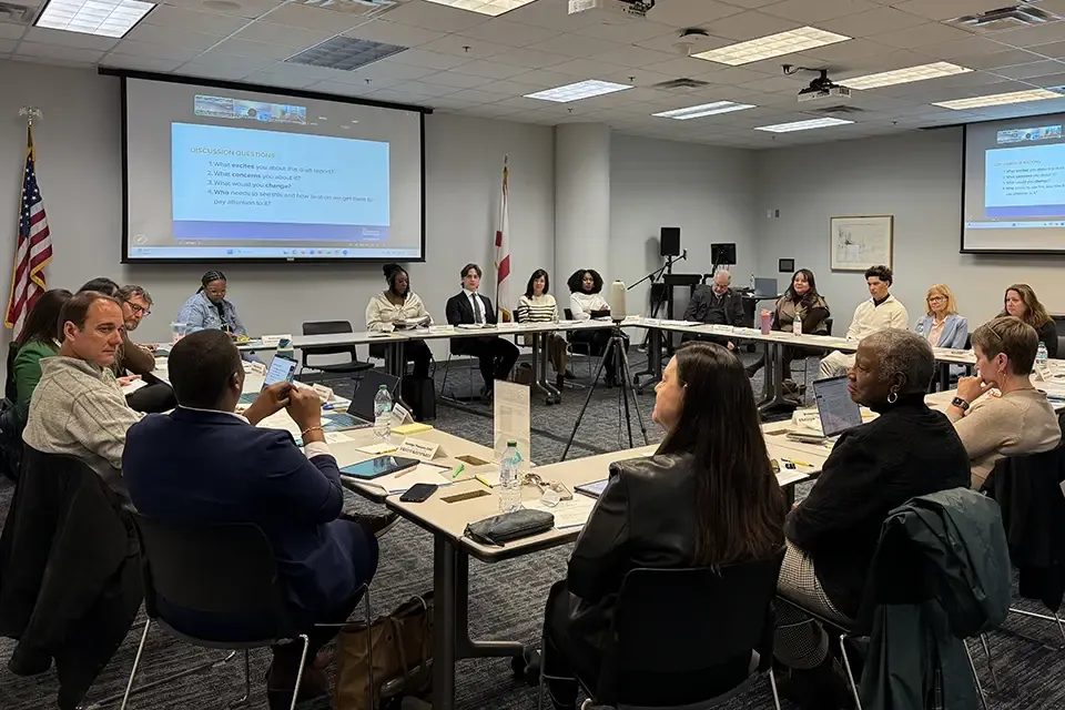 Group of council members seated around a U-shaped conference table during a Children's Week meeting in Tallahassee, with documents and water bottles visible.